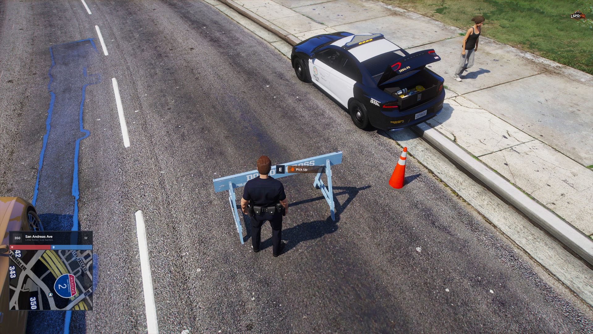 Officer facing a deployed blue police barrier with the E Pick Up prompt visible